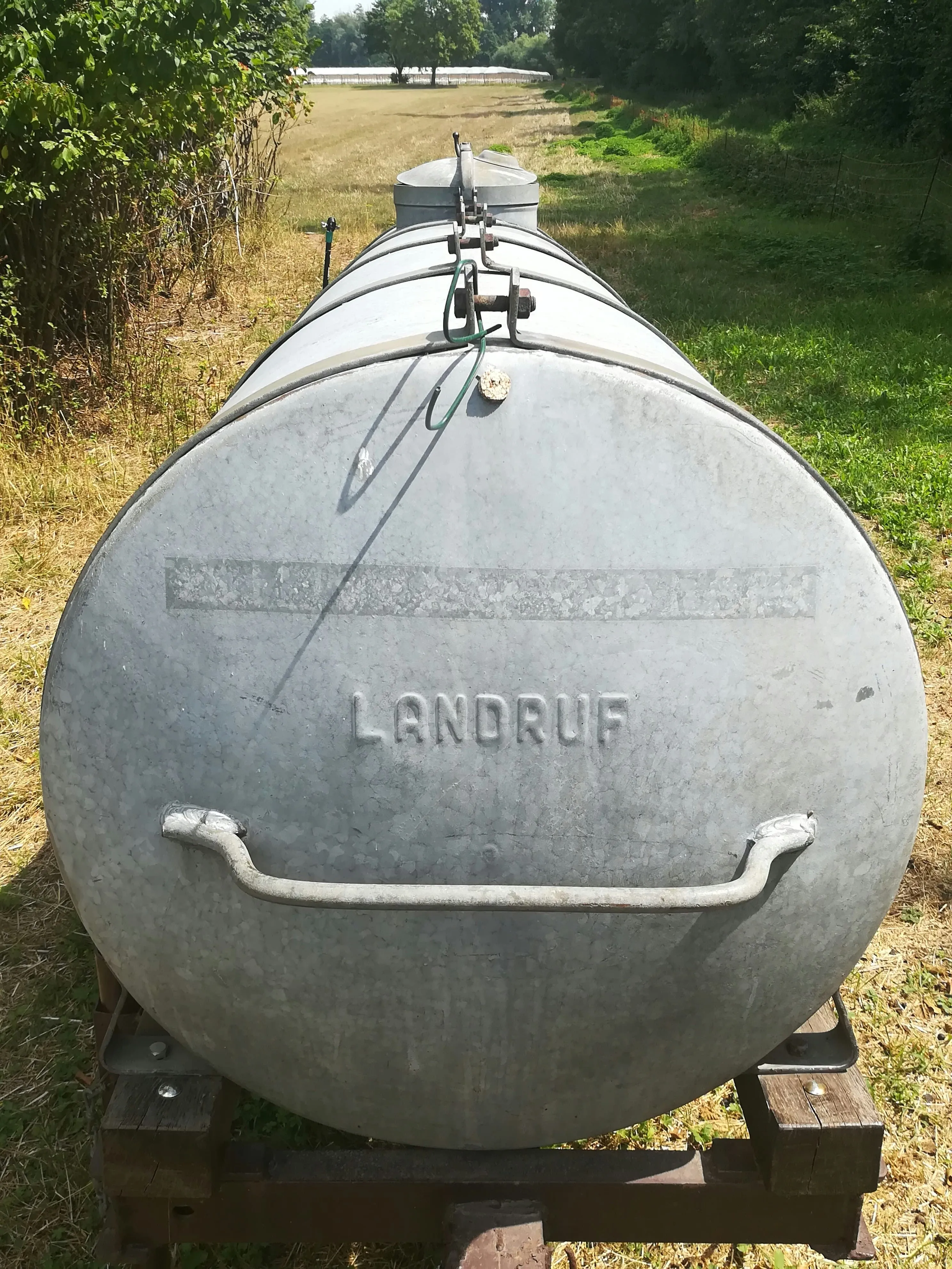 A large galvanized steel water tank in a field, representing clean freshwater supply for mobile units