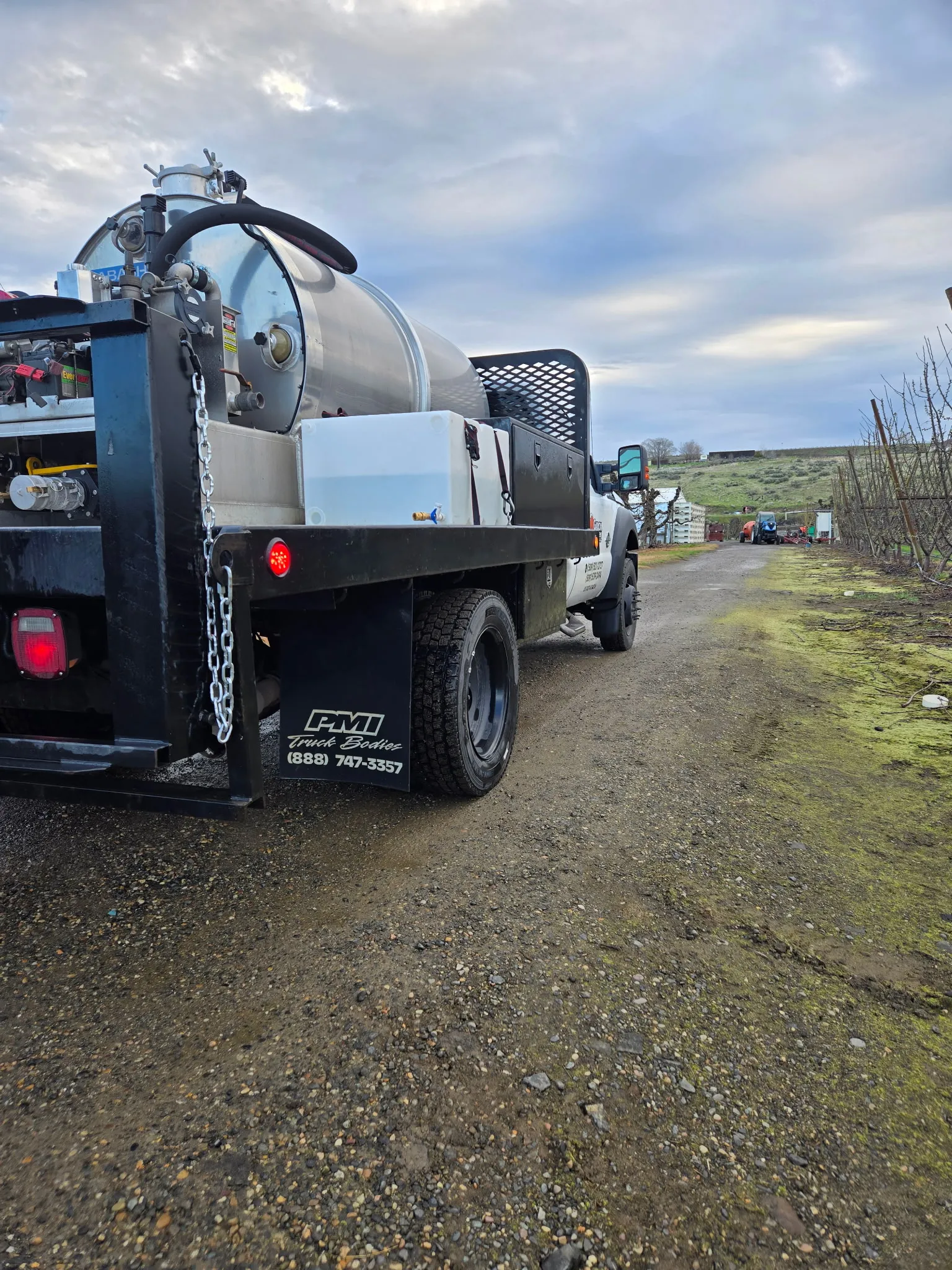The rear of a Garcia Brothers pump truck fitted with a polished stainless-steel waste tank, parked on a gravel service yard under a cloudy Tri-Cities sky