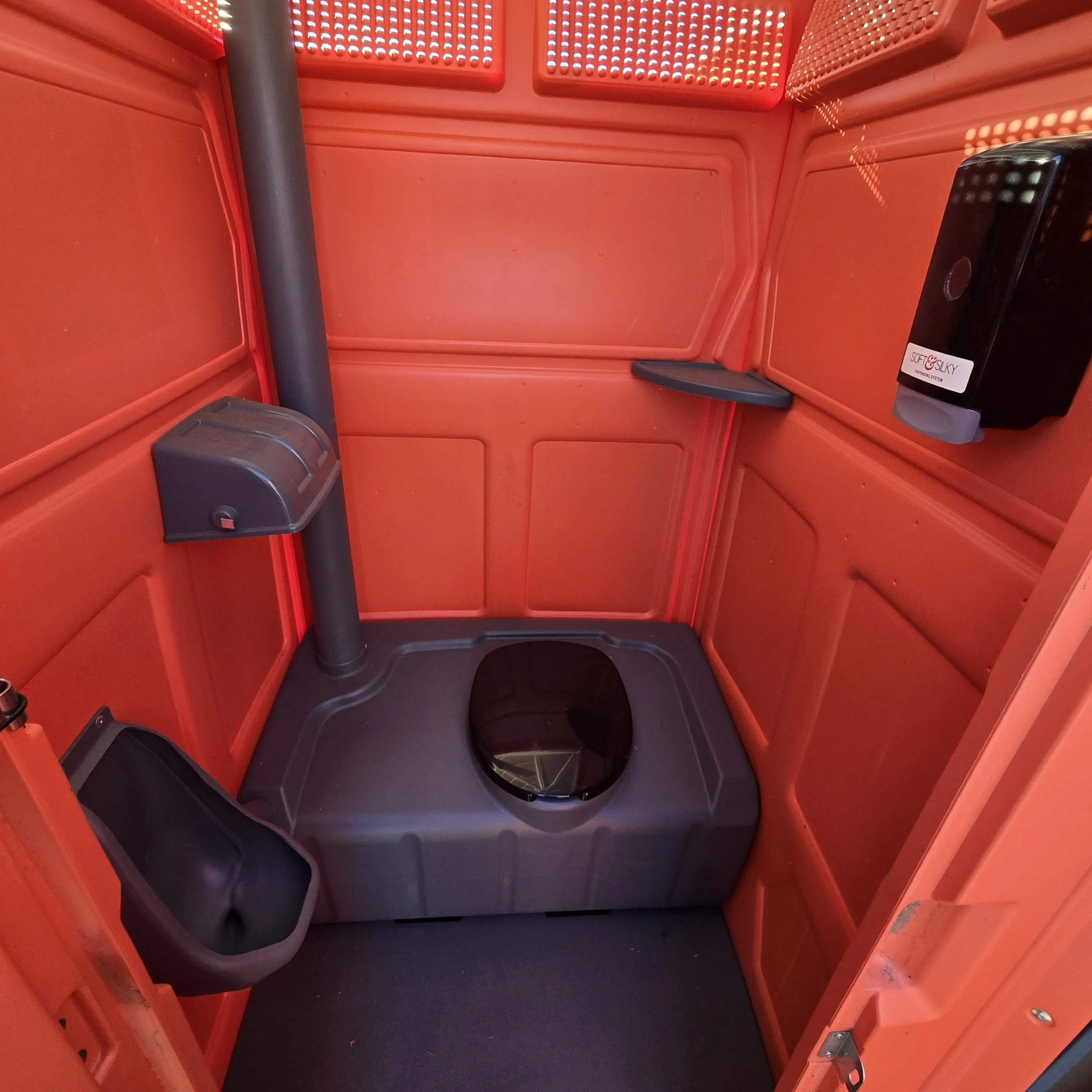 The clean interior of a standard Garcia Brothers portable toilet, showing the urinal and built-in hand sanitizer dispenser