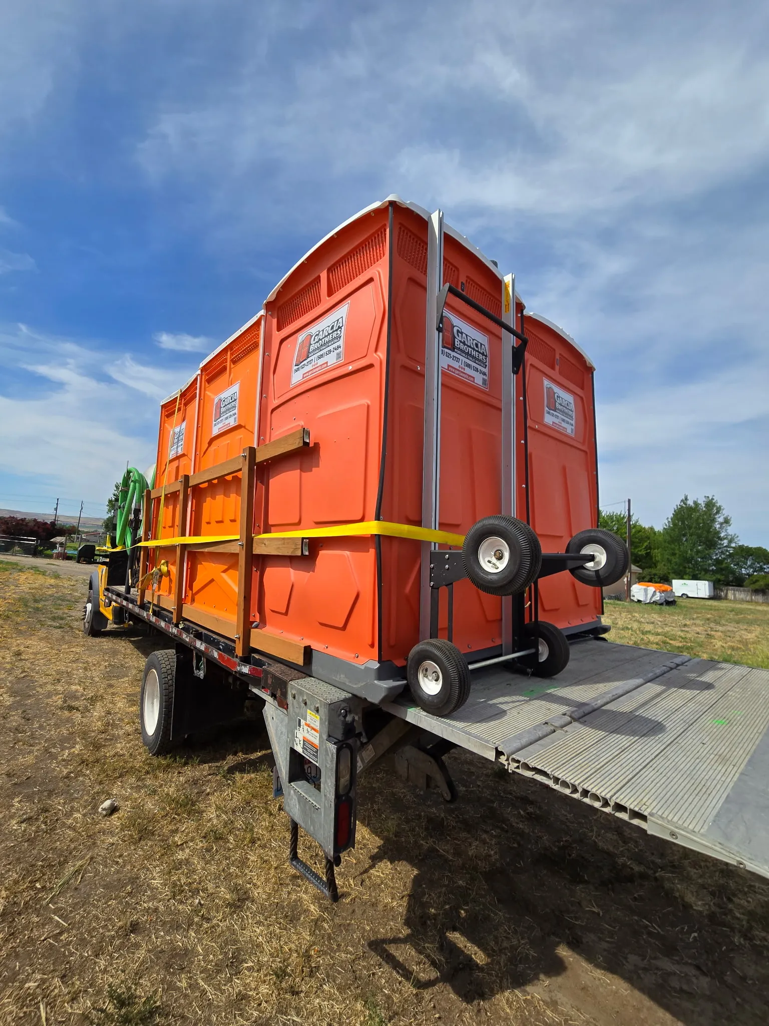 A flatbed trailer loaded with several orange Garcia Brothers portable toilets, strapped down and ready for delivery across the Tri-Cities